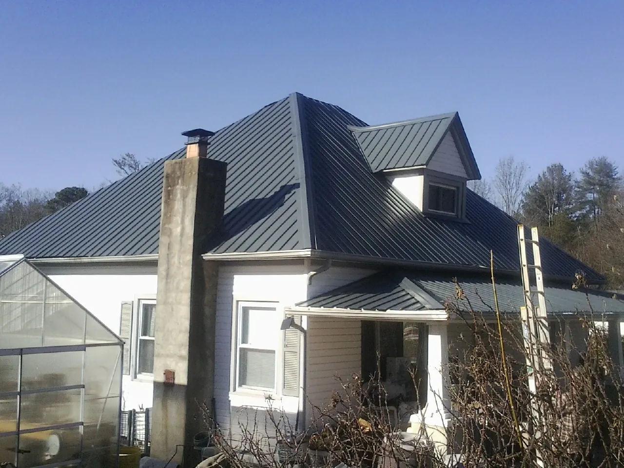 Dark blue standing seam metal roof on a white farmhouse with dormer — Slate & Tile Roof Repair by Roofing Brothers in Kenbridge