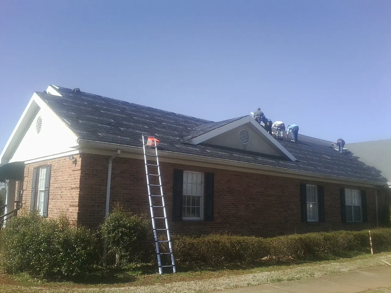 Crew tearing shingles off a brick ranch roof with a ladder set — Metal Roof Repair work by our crew in Kenbridge