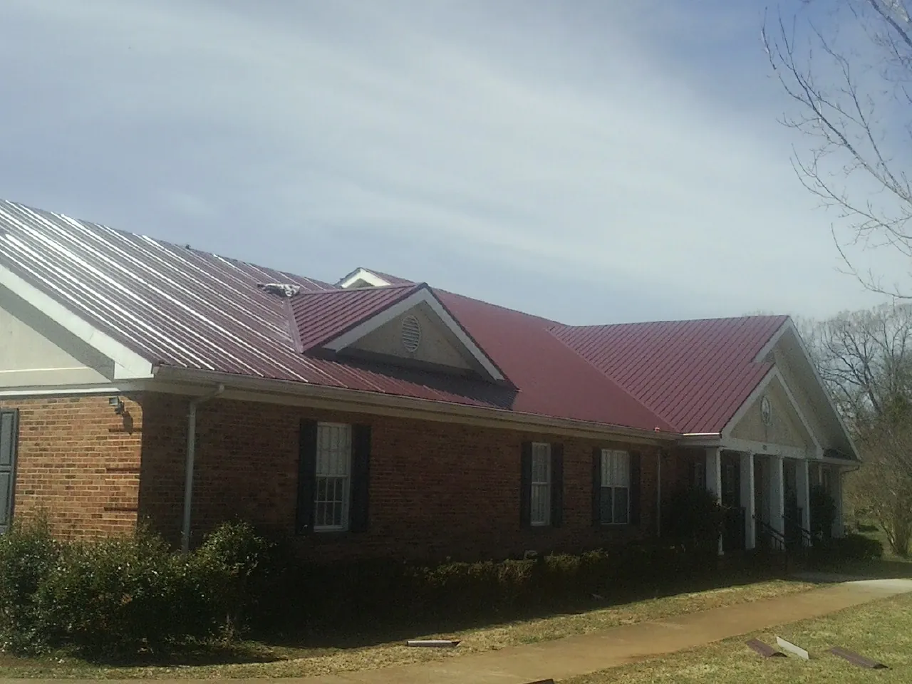 Red metal roof with gabled entries on a long brick building, from a Hail Damage Roof Repair job in Kenbridge
