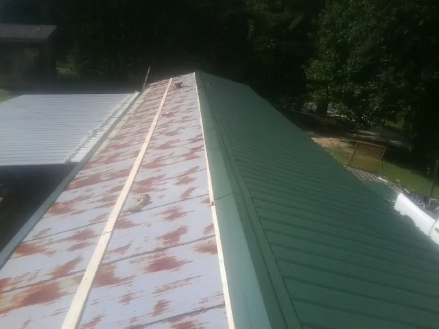 Old rusted panels beside newly installed green metal roofing — Wind Damage Roof Repair by Roofing Brothers in Kenbridge